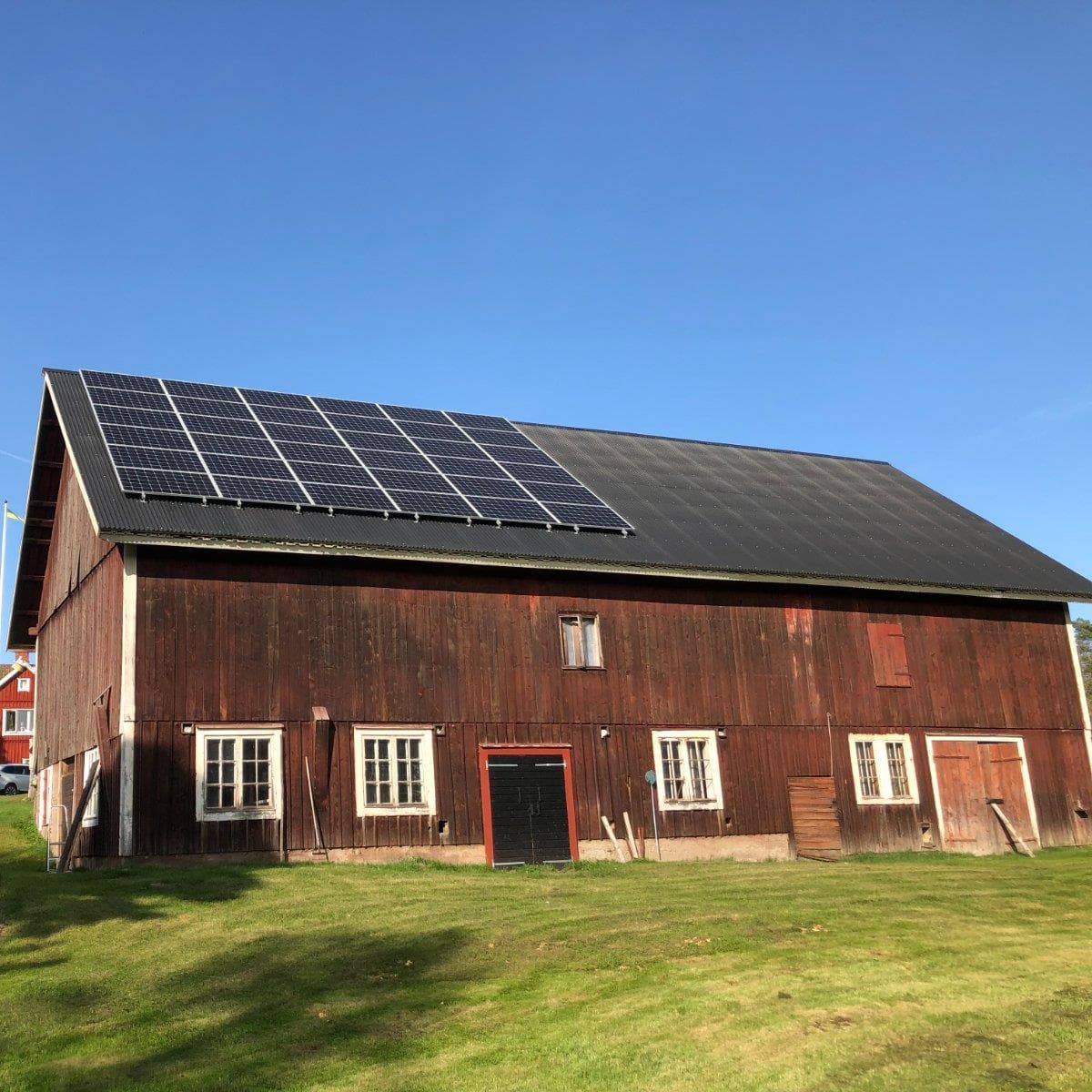 Äldre träförråd med solpaneler installerade på taket under klarblå himmel