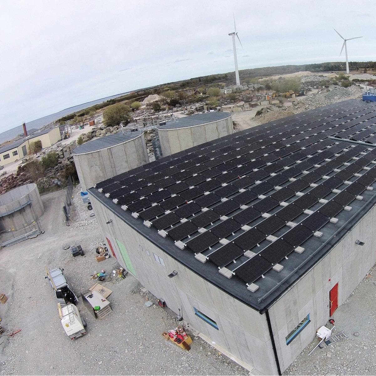 Solpaneler på avsaltningsstationens industribyggnad i Sandvik med vindkraftverk i bakgrunden