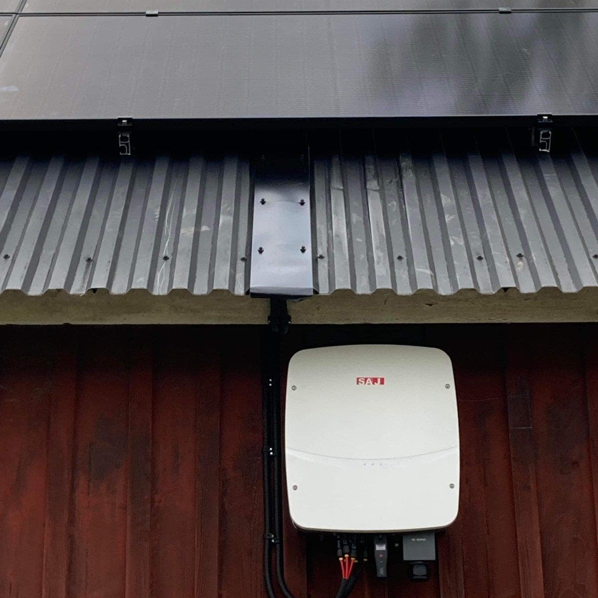 Solpaneler på ett korrugerat plåttak med en växelriktare på träväggen nedanför