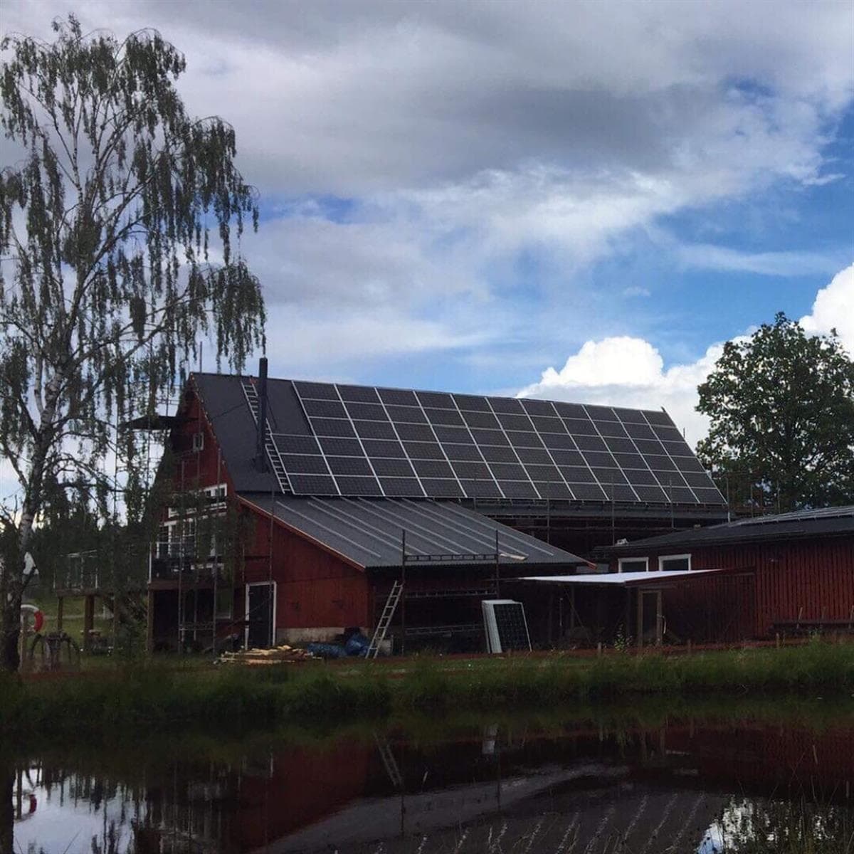 Stall Annebergs röda byggnad med färdiga solpaneler speglad i en damm