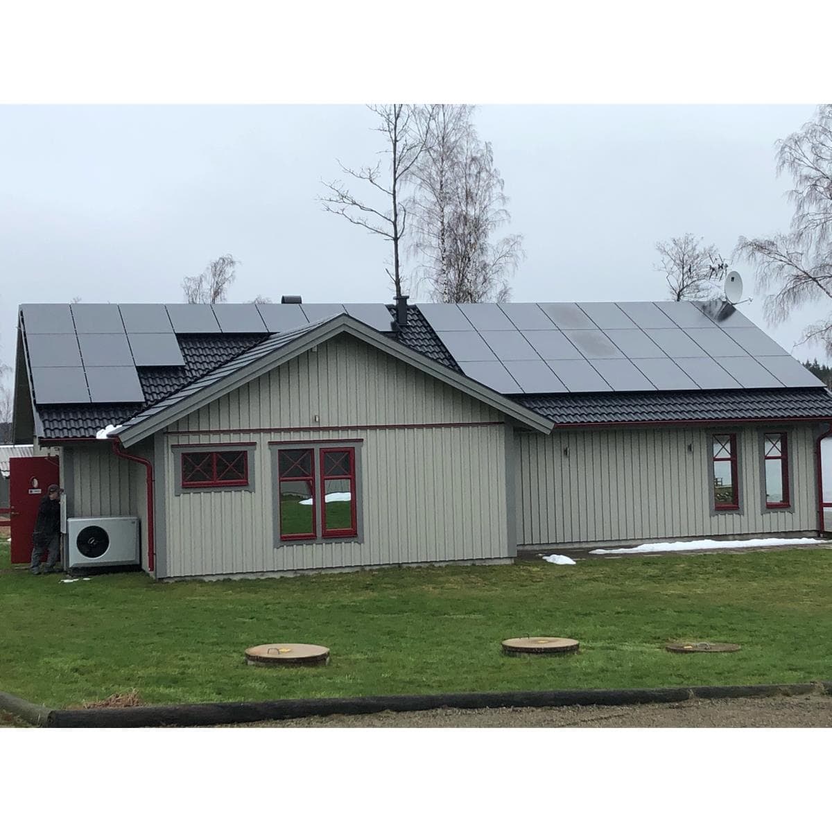 Stuga med beige träfasad, röda detaljer och solpaneler på taket