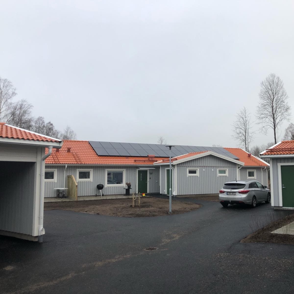 Enplanshus med solpaneler på rött tegeltak och carport intill