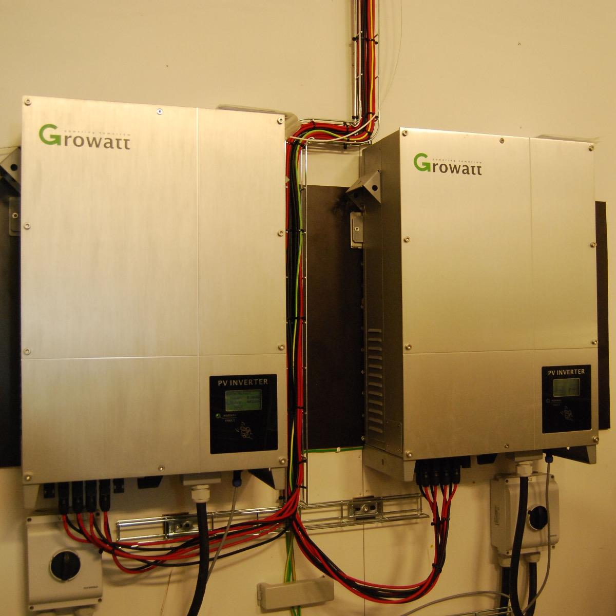 Två Growatt PV-växelriktare monterade på en vägg, anslutna med färgglada ledningar, som används för att omvandla solenergi.