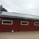 Röd byggnad med korrugerat tak med solpaneler. Mulen himmel och en skottkärra nära byggnaden.