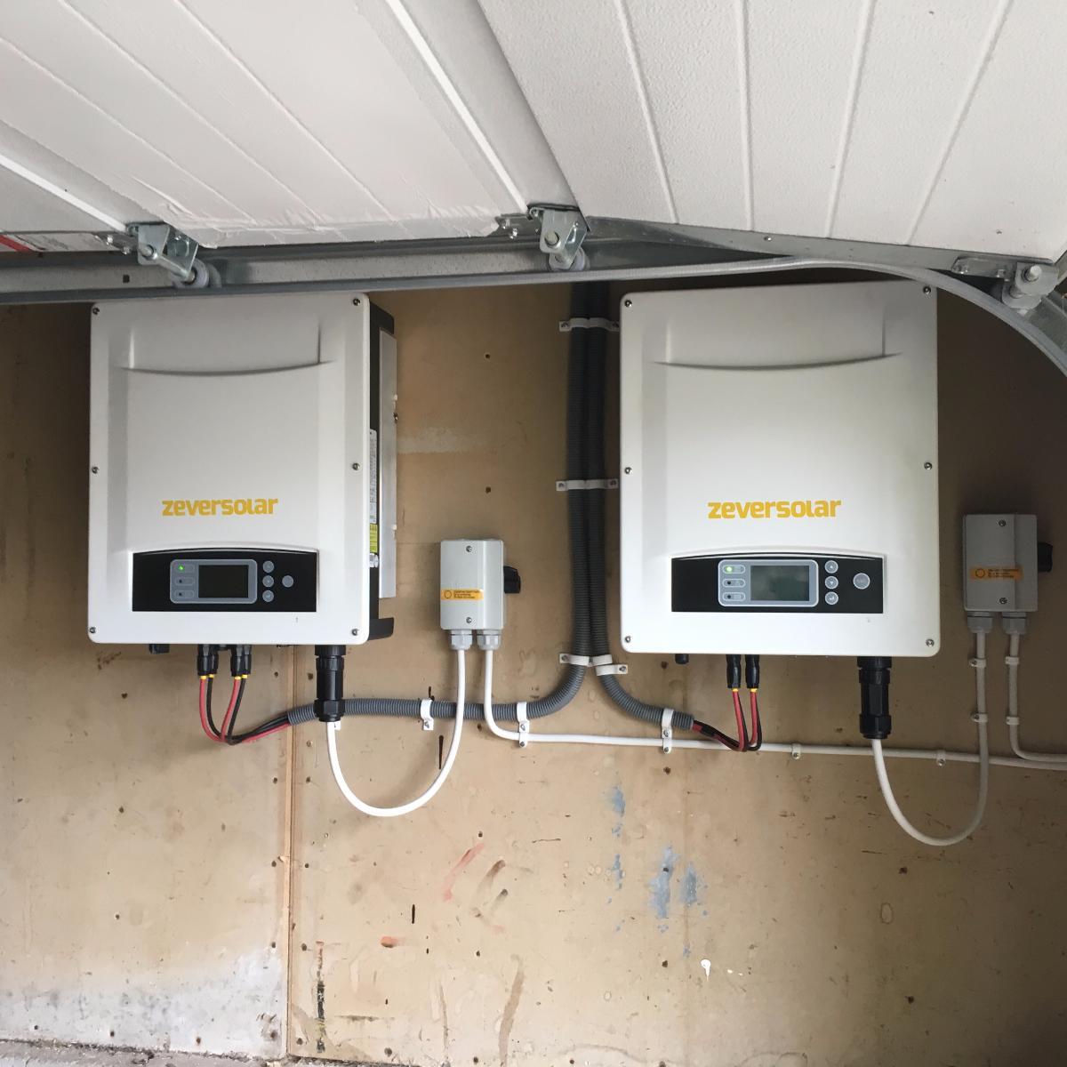 Väggmonterade solcellsväxelriktare från ZeverSolar med displayer, anslutna med ledningar, installerade i ett garage eller bruksområde.