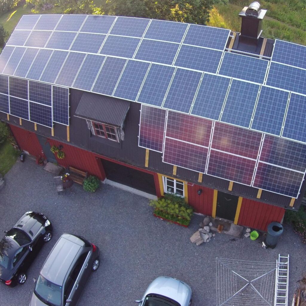 Flygfoto över ett hus med solpaneler som täcker taket. Flera bilar står parkerade utanför på uppfarten.