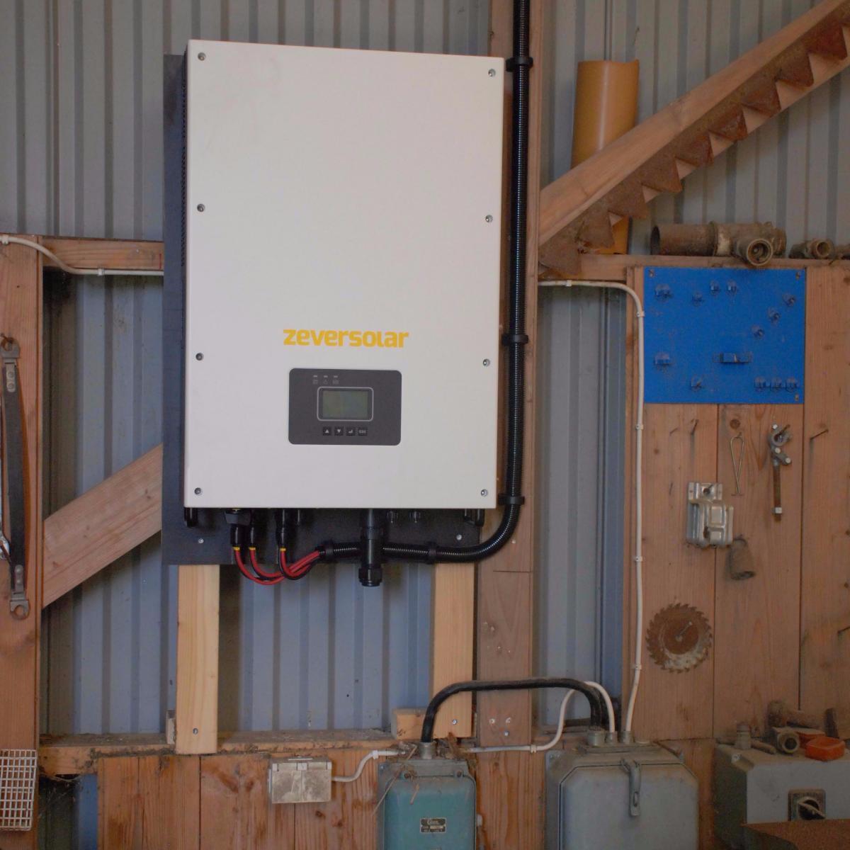 En väggmonterad Zeversolar inverter med digital display, omgiven av olika verktyg och utrustning i en verkstad.