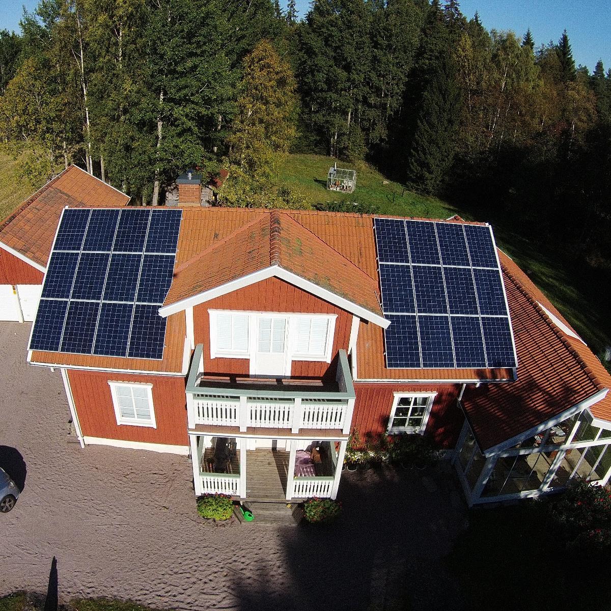 Ett rött hus med solpaneler på taket, omgivet av träd och en trädgård.