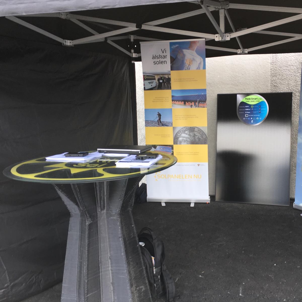 Informationsbås med ett runt bord uppställt under ett tak. Displaybanderoller och informationsbroschyrer står uppställda på bordet.