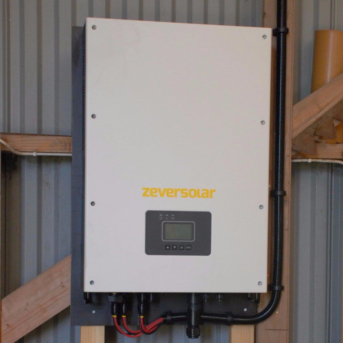 En Zeversolar solcellsinverter monterad på en träram inne i en byggnad, med synliga kablar och en liten bildskärm.