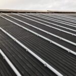 Metalltak med jämnt fördelade silverskenor för installation av solpaneler, sett från låg vinkel. Mulen himmel i bakgrunden.