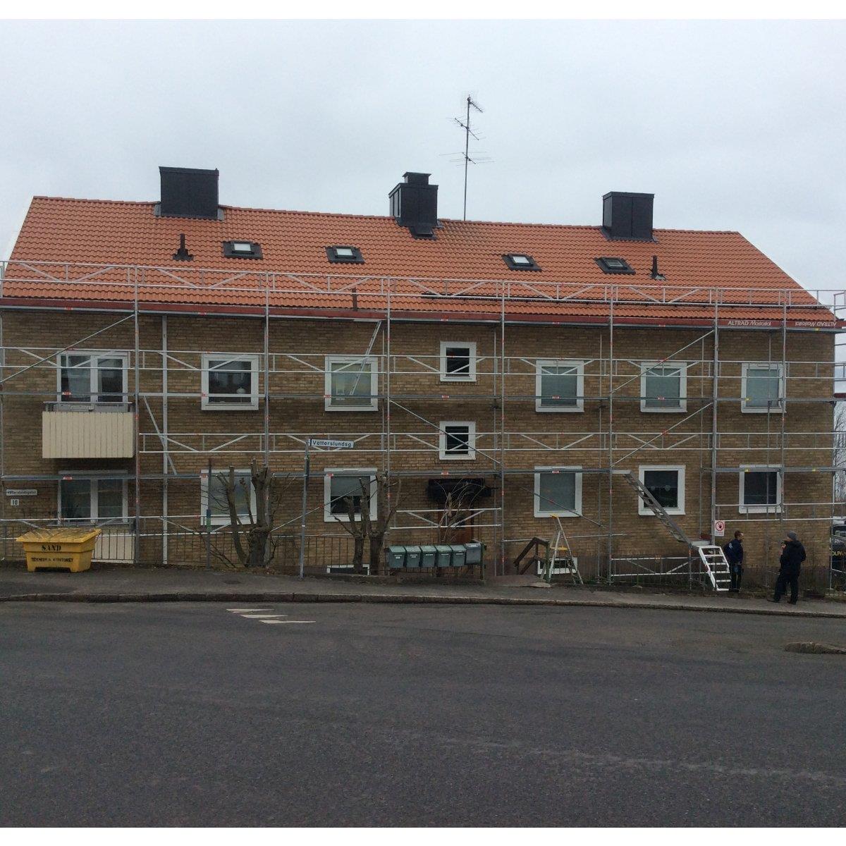 En tvåvånings tegelbyggnad med ställningar som täcker framsidan. Det finns små fönster och ett rött tegeltak. En person står nära det högra hörnet.