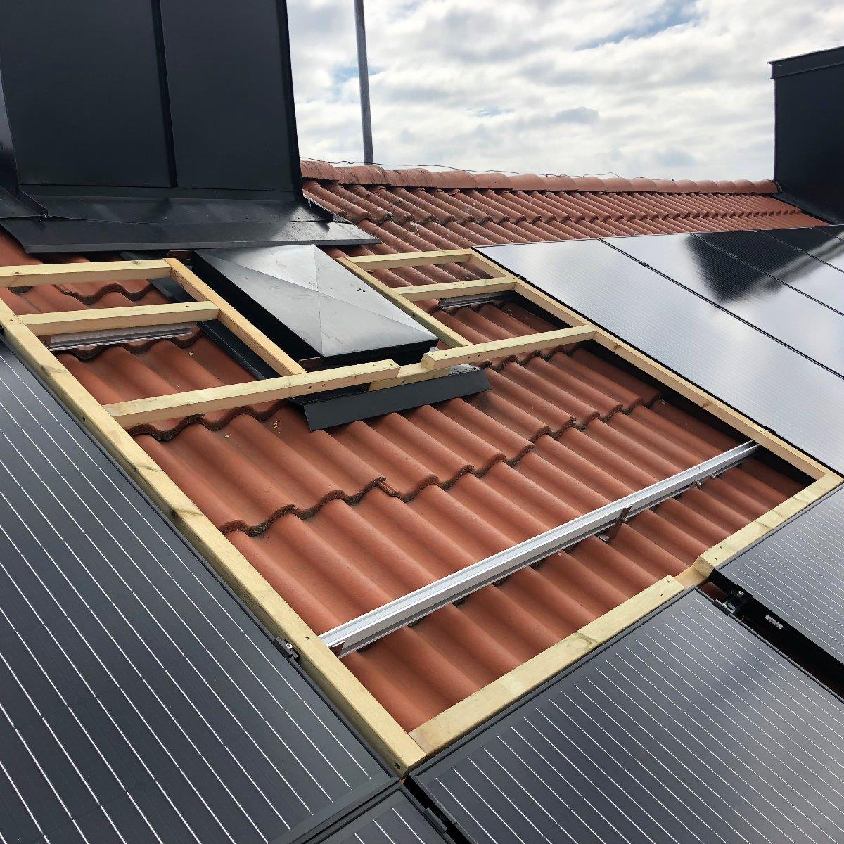 Solpaneler installeras på ett rött tegeltak, med några paneler som saknas och luckor avslöjar träram under mot en molnig himmel.