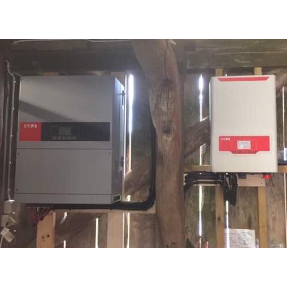 Två elektriska växelriktare monterade på en trävägg, med kablar som förbinder dem.