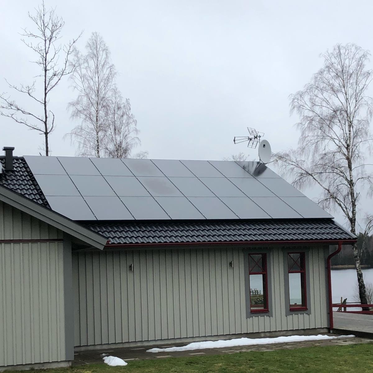 Ett hus med solpaneler på taket, omgivet av träd en molnig dag.