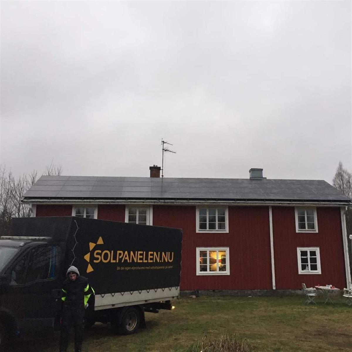 Ett rött hus med solpaneler på taket. Framför står en lastbil med Solpanelen.nu tryckt på sidan. En person står nära lastbilen.