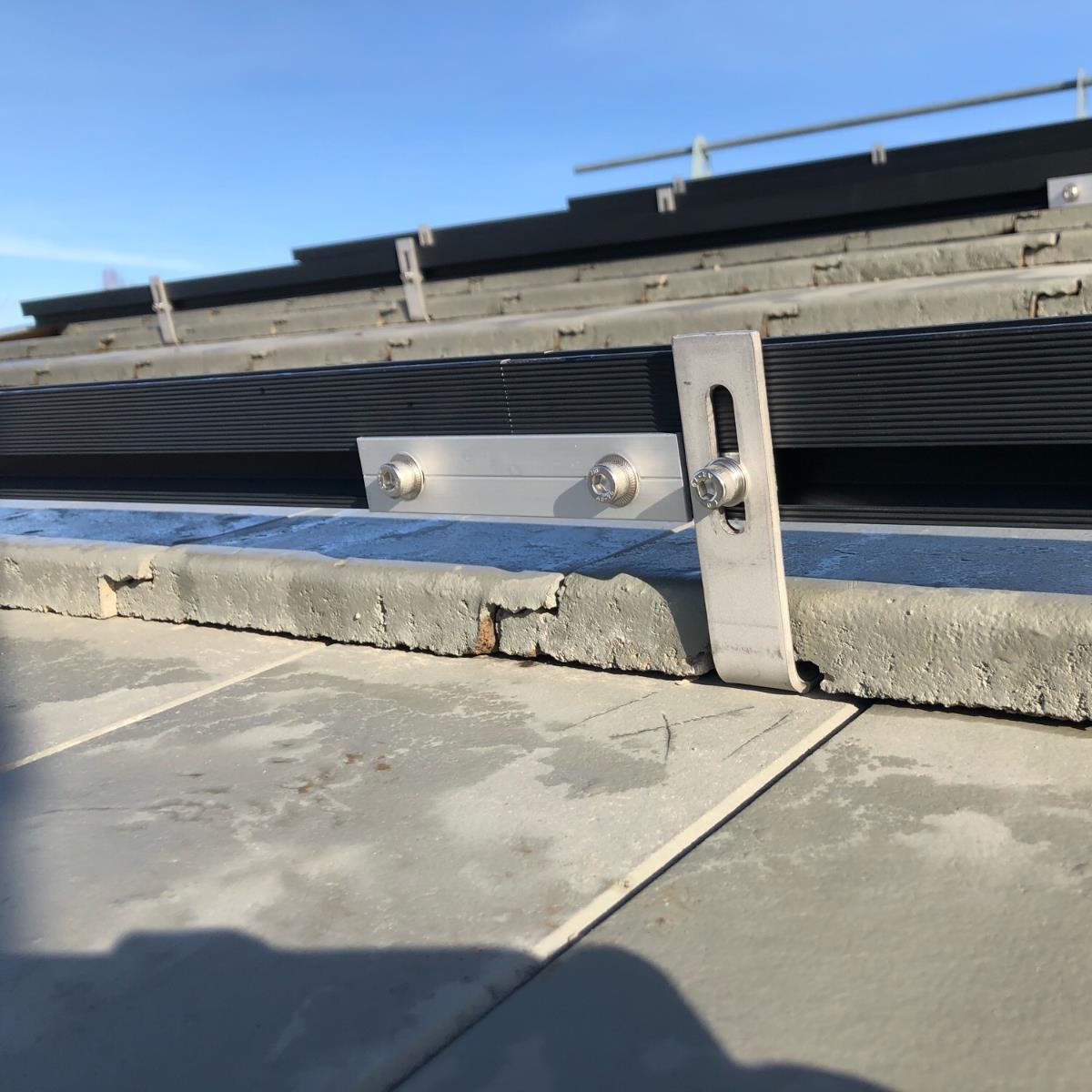 Närbild av ett monteringsfäste för solpaneler fäst på ett tak med bultar på en solig dag.