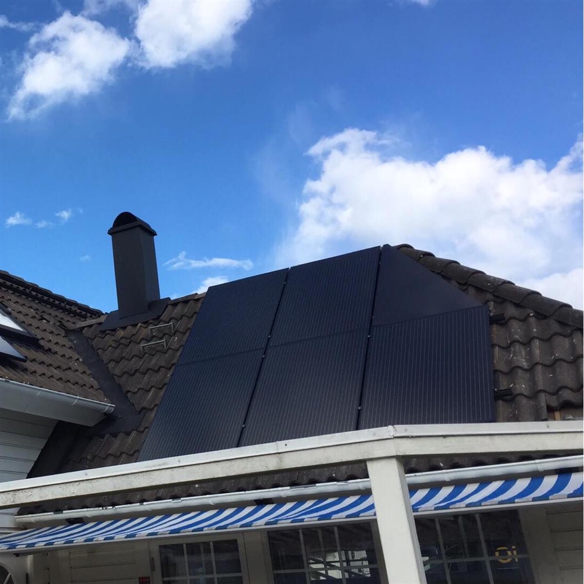 Ett tak med sex solpaneler installerade, under en delvis molnig himmel. Det finns en skorsten till vänster och en randig blåvit markis.