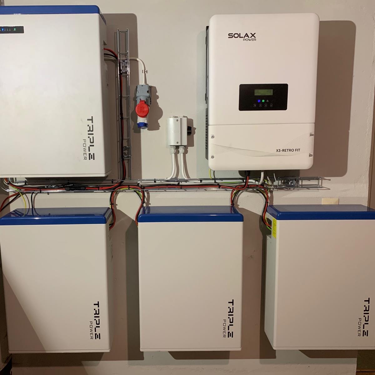 Väggmonterad solenergiomriktare och tre batterilagringsenheter anslutna med synliga kablar.