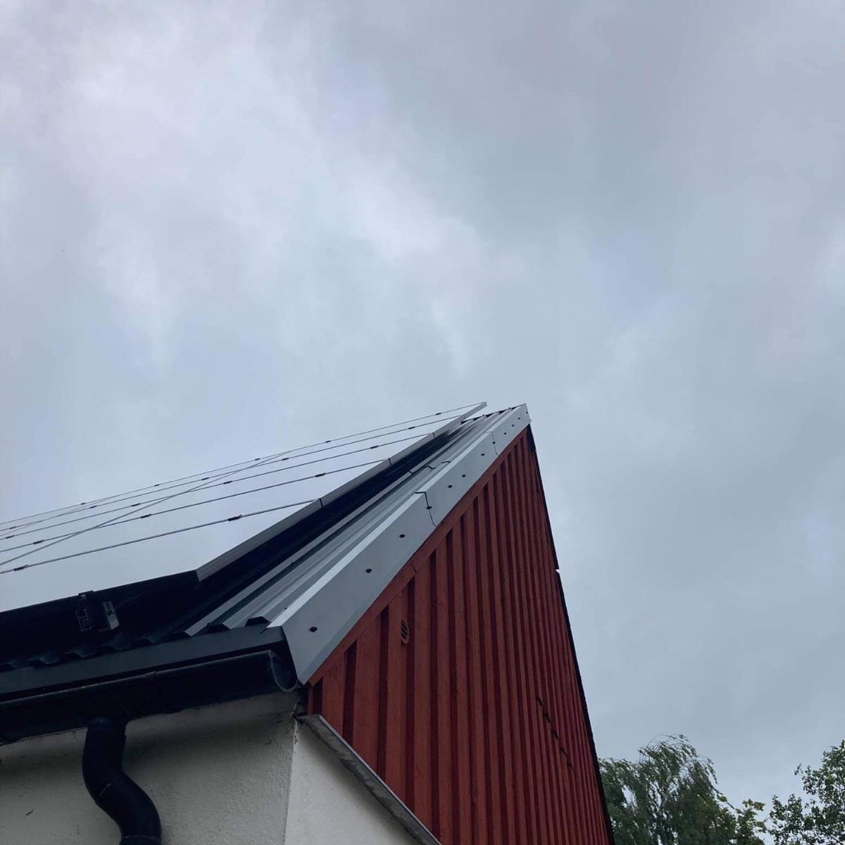 Takhörn med solpaneler på en röd och vit byggnad, under en molnig himmel.