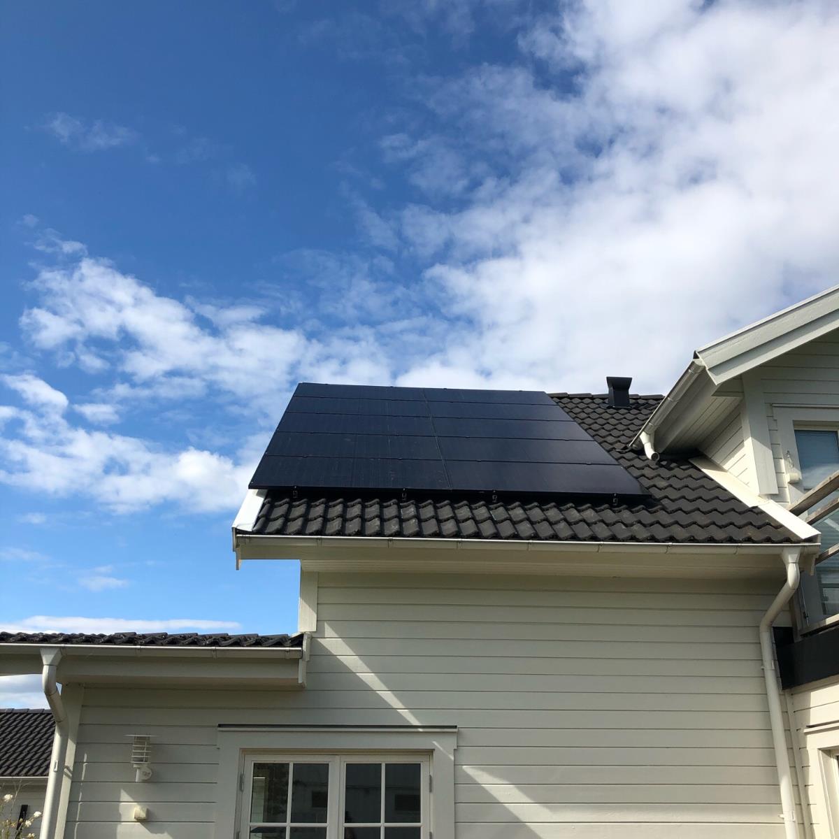 Solpaneler installerade på taket av ett ljust hus under en delvis molnig himmel.